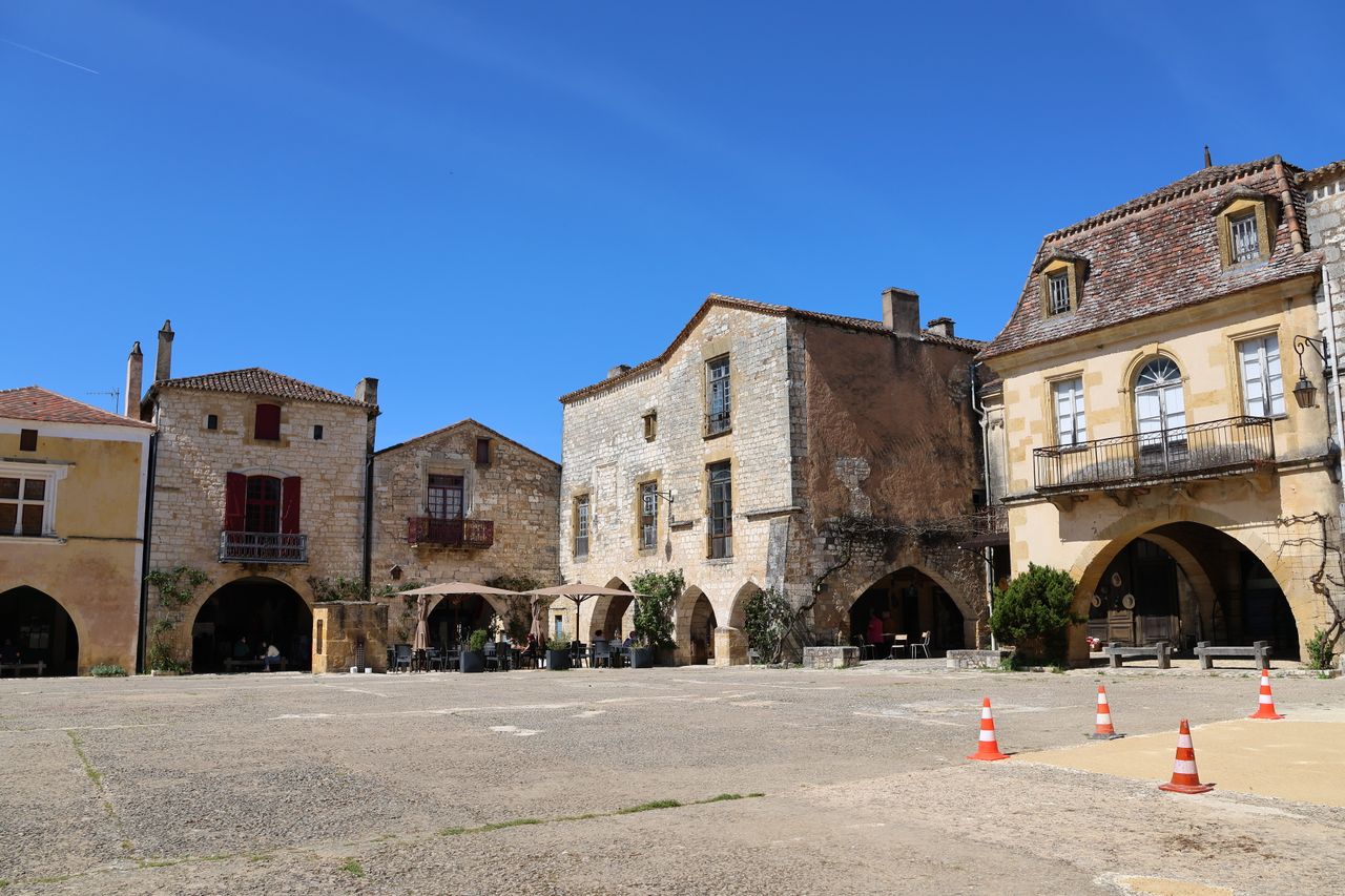 Charming stone buildings lining a sunlit plaza in a historic French village.