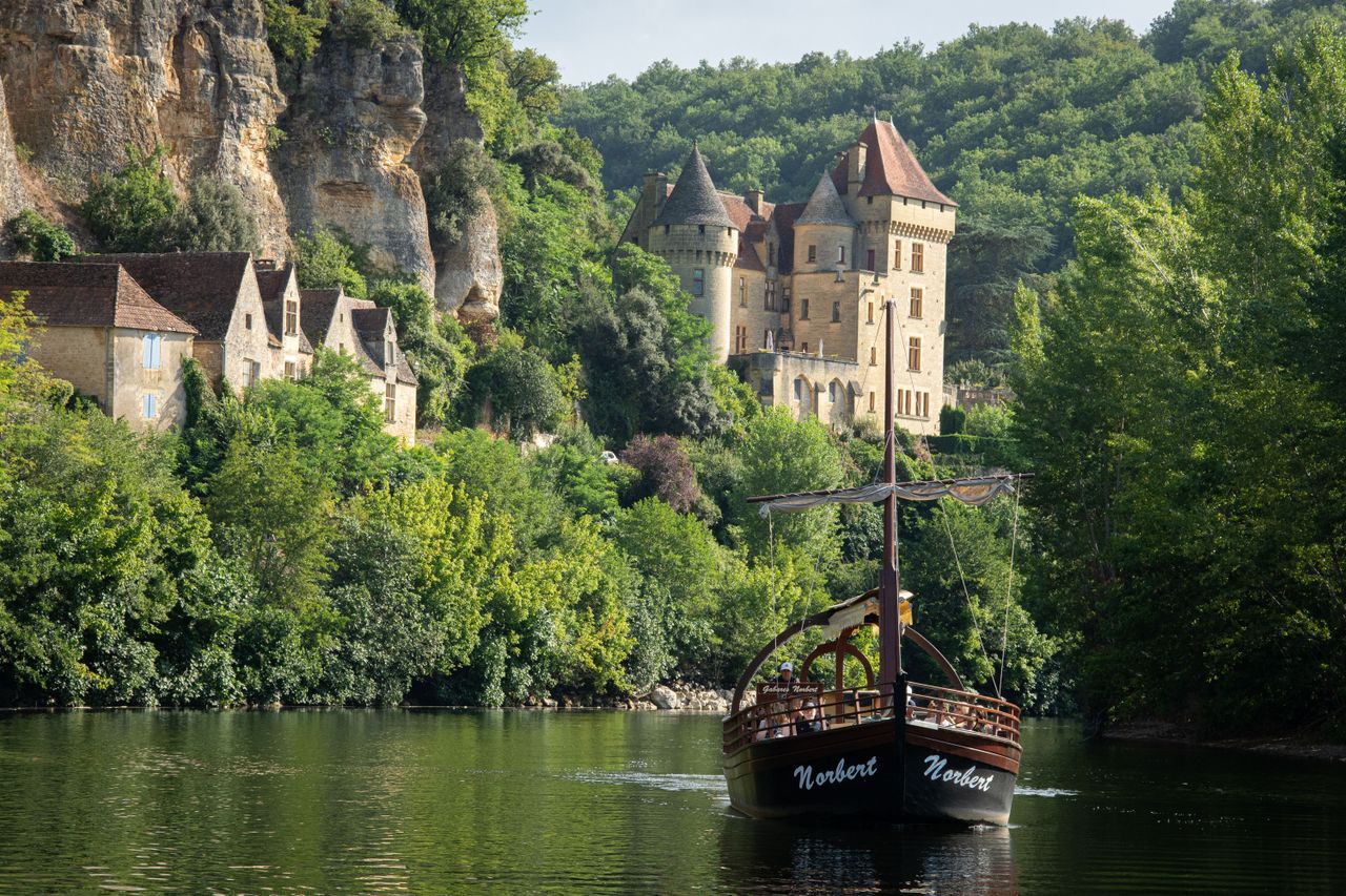 Charming boat on Dordogne River near a medieval castle in Nouvelle-Aquitaine, France.